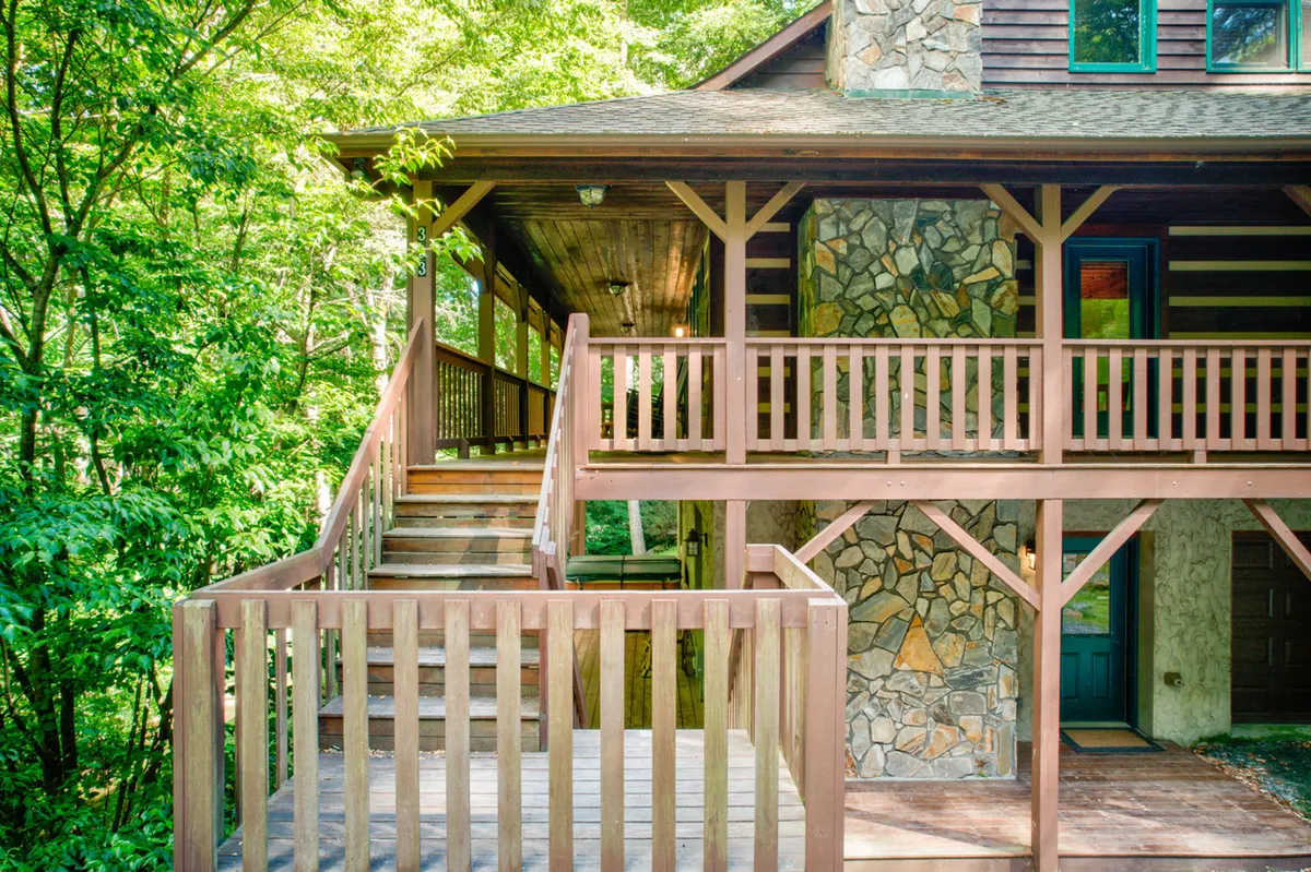 This exterior shot shows a sturdy wooden staircase, stone wall, and balcony railings, set against a backdrop of greenery. The elevated perspective hints at panoramic views and the ability to enjoy both sunrise and sunset from the balcony, as well as easy access to the outdoors for hiking and exploring.