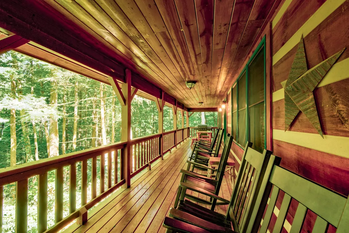 A welcoming interior porch scene featuring sturdy wooden rocking chairs lined up along a wooden railing. Natural light streams in through the windows, illuminating the cozy space, while a decorative star adds a touch of mountain charm.