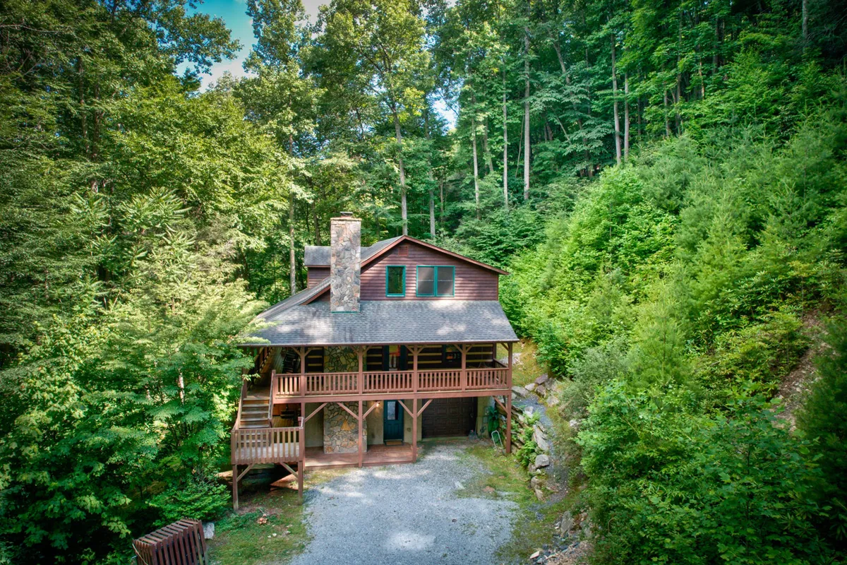 The photo captures Little Creek Lodge’s rustic wooden façade with a stone accent, surrounded by trees and a gravel driveway. The inviting porch hints at a welcoming gathering spot perfect for group arrivals and outdoor enjoyment.