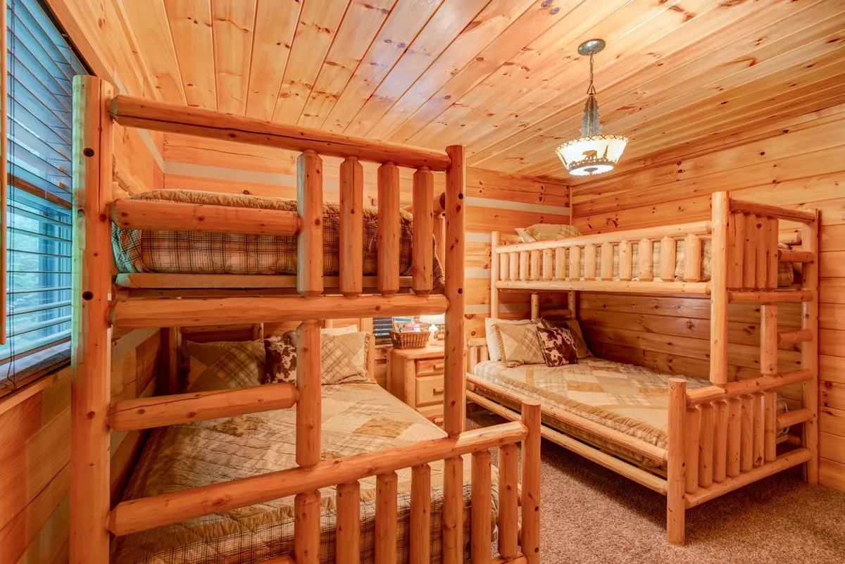 A dedicated bunk room with two sets of sturdy wooden bunk beds, warm wood paneling, plaid bedding, and an ornate light fixture overhead. The room feels inviting and playful, perfect for kids or groups.