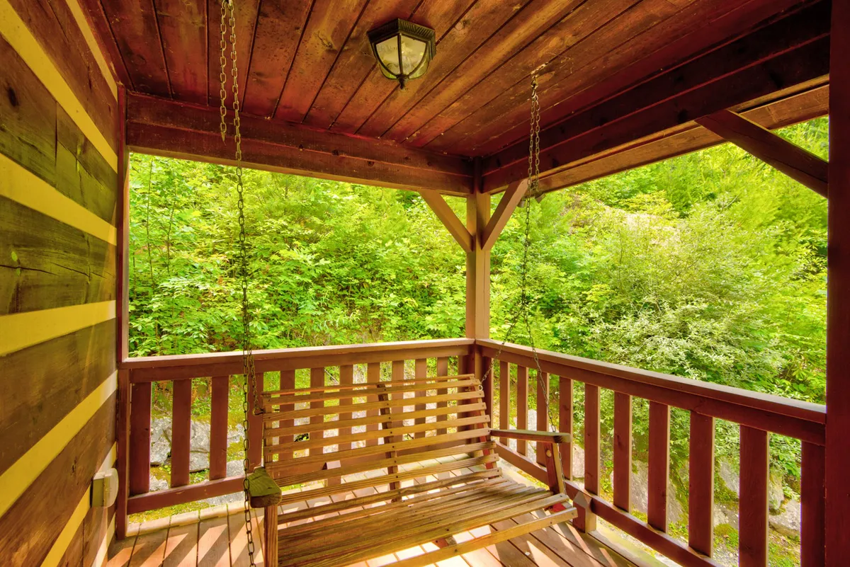 This image features a swinging bench on a wooden porch, framed by green foliage. The surrounding trees and open air create a serene and immersive outdoor experience, ideal for unwinding after a day of hiking or exploring. The view suggests a close connection to nature and opportunities for stargazing or listening to the creek.