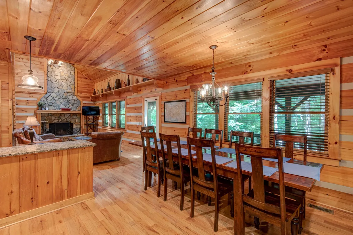 A spacious dining area with a central wooden table, striking chandelier, a stone fireplace, and large windows providing scenic views. The setup is ideal for family gatherings or relaxing after a day spent exploring the High Country.