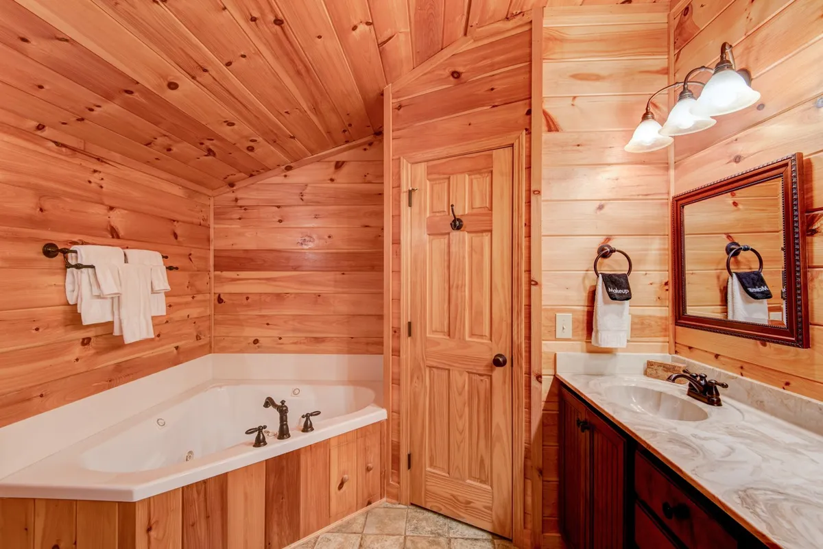 A tranquil bathroom retreat with a large corner Jacuzzi tub, double sink vanity, wooden cabinetry, and wood-paneled walls. The lighting is soft, creating a serene atmosphere perfect for relaxation.