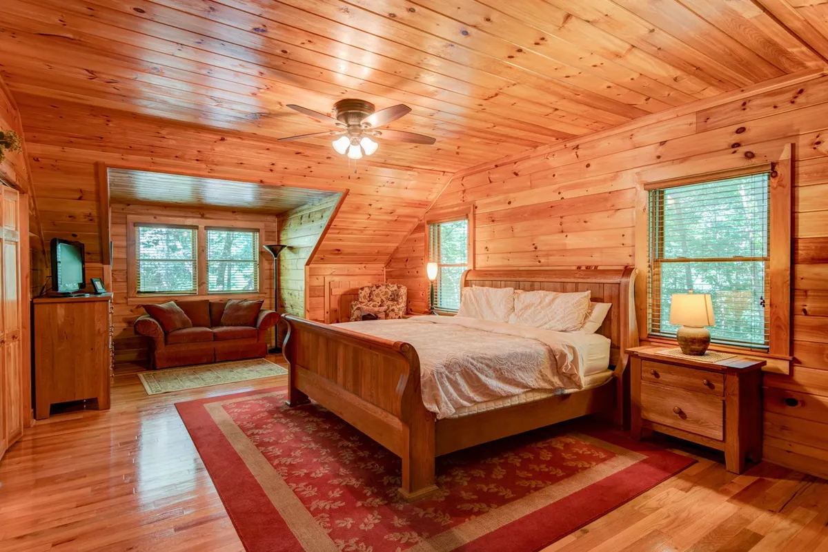 A serene bedroom featuring a wooden bed, nightstand with lamp, sofa, and windows that frame natural views. The soft lighting and intimate layout create a tranquil, romantic setting ideal for couples seeking relaxation and privacy.